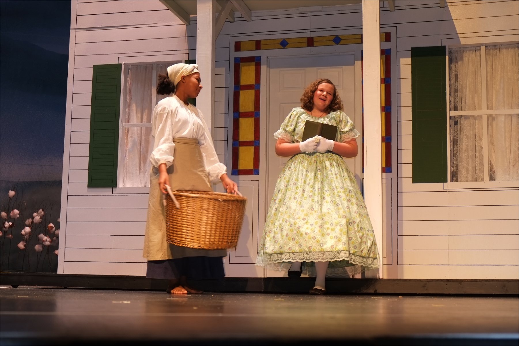 Two young female actresses on stage portraying a slav and Plantation owner daughter in a play about the Underground Railroad.