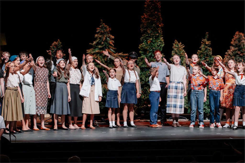 Group of young actors and actresses performing the last scene of a play set on the Oregon trail